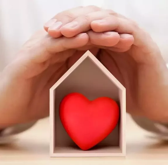 Symposium sur la sécurité émotionnelle : des mains sur une petite maison en bois dans laquelle se trouve un cœur rouge
